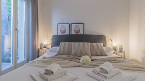 Een keurig opgemaakt bed met handdoeken, een hoofdbord en twee ingelijste foto’s aan de muur.