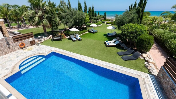 A swimming pool with a view of the sea, surrounded by a well-maintained lawn and lounge chairs.