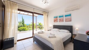 A bedroom with a bed, a nightstand, a desk, a chair, a window with curtains, and a view of the outdoors.
