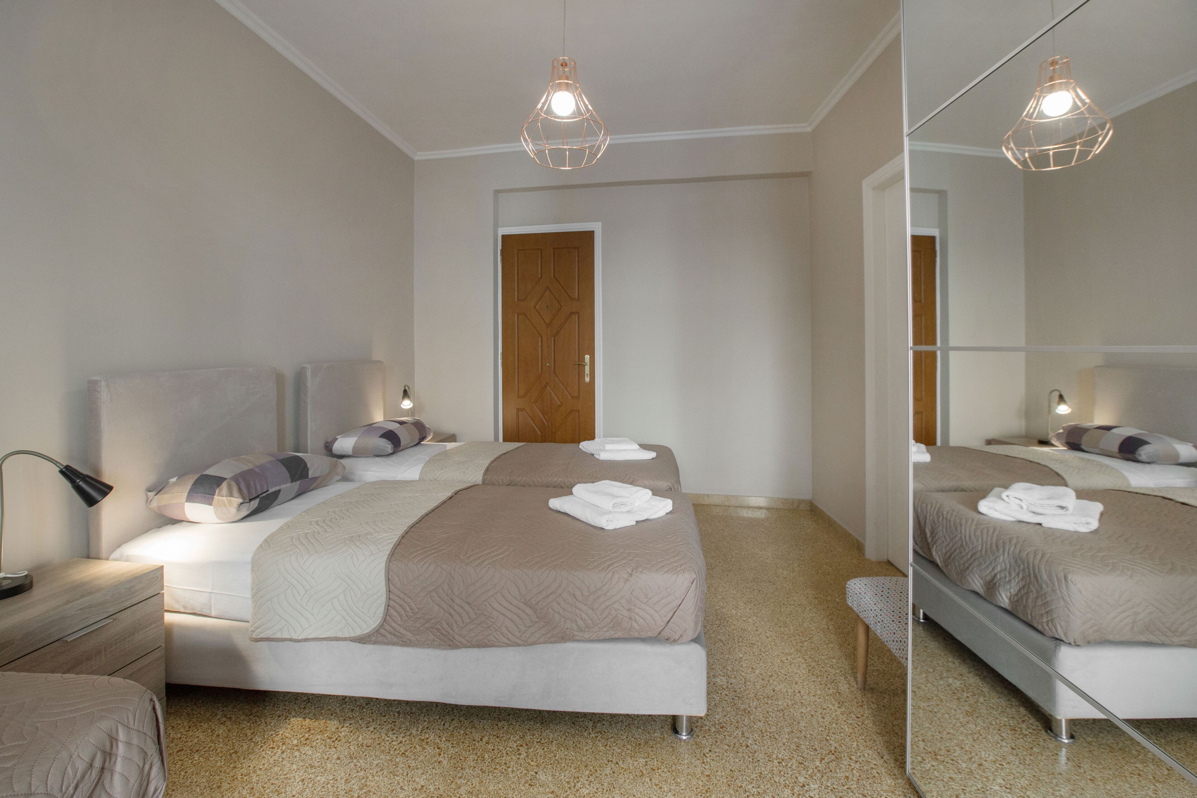 Une chambre d’hôtel avec deux lits, une porte en bois, un miroir et un luminaire au plafond.