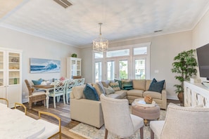 A spacious living room with a large sectional sofa, a dining table with chairs, and a chandelier.