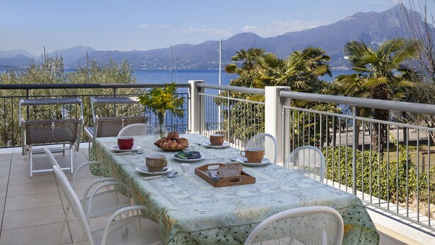 Un balcon avec une table préparée pour le petit-déjeuner, offrant une vue panoramique sur la mer et les montagnes.