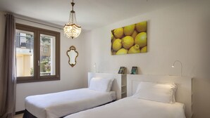 Une chambre d’hôtel avec deux lits, un lustre, une fenêtre avec des rideaux, un miroir et un tableau représentant des citrons.