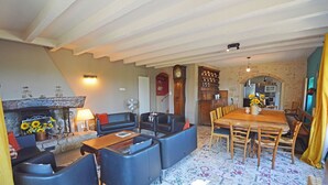 Una sala de estar acogedora con chimenea, un comedor con mesa y sillas de madera, y una cocina visible a través de un arco.