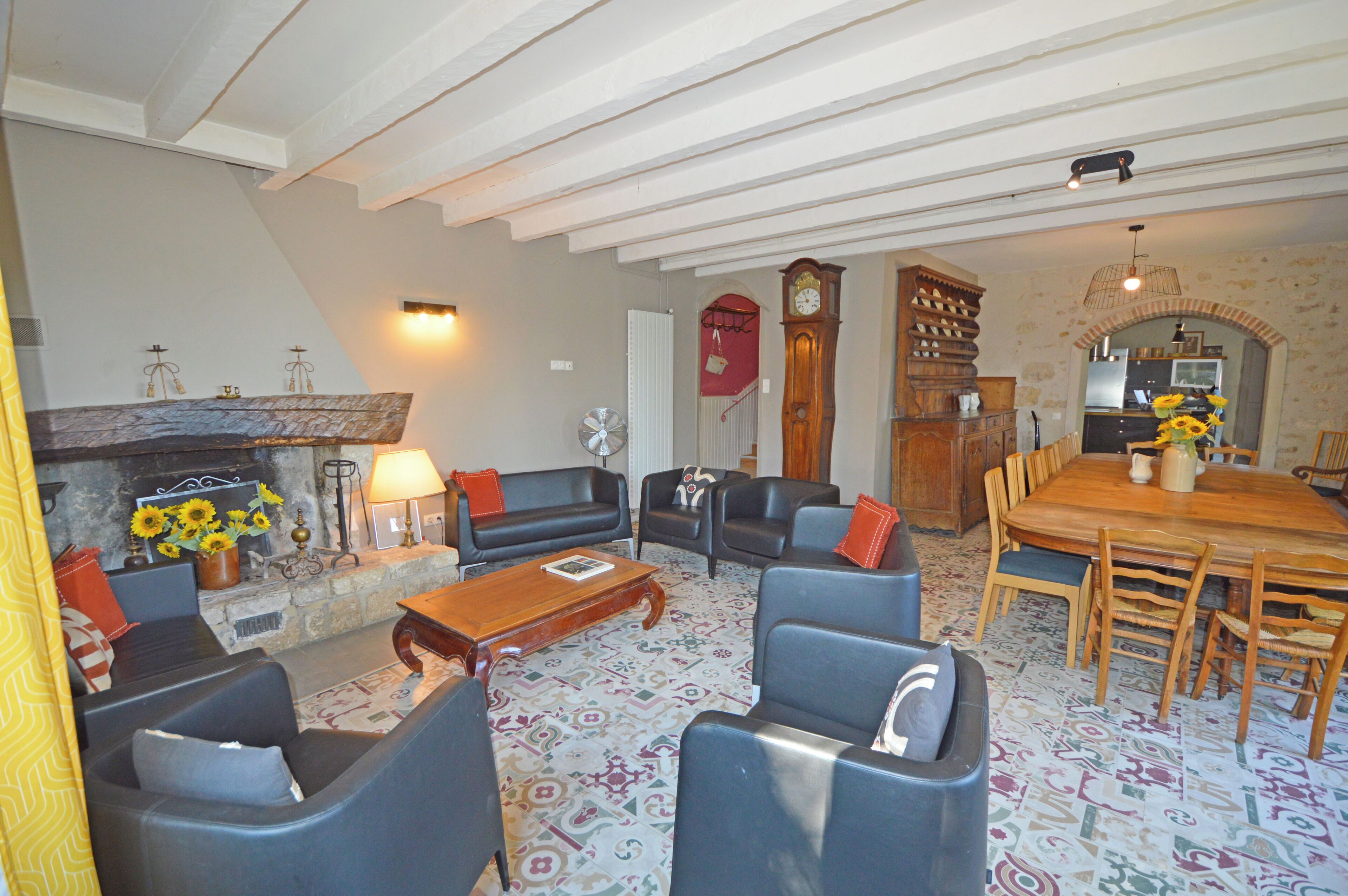 Een woonkamer met een open haard, banken, een eettafel met stoelen, en een keuken die door een boog zichtbaar is.