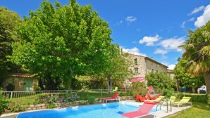 Una piscina con sillones reclinables rojos y verdes, rodeada de follaje y un edificio de piedra.