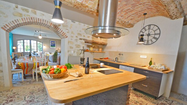 Una cocina con una isla de madera, un arco de ladrillo y un reloj grande en la pared.