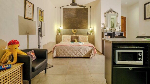 A bedroom with a bed, a black sofa, a wooden side table, a ceiling fan, a wall-mounted TV, and a microwave. - Camaella Luxury Studio (Vernazza)