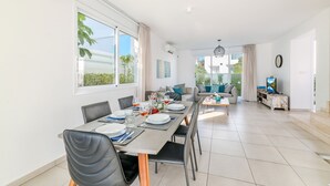 Un comedor moderno con una larga mesa preparada para seis personas, un sofá y un televisor al fondo.