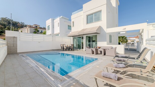 Un área de piscina moderna con una piscina cristalina, sillones de descanso y una mesa con sillas.