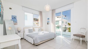 Un dormitorio moderno con una cama grande, un escritorio y una silla. Hay un balcón con vistas a edificios.