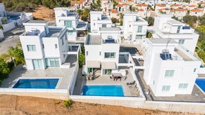 Un moderno complejo residencial con varios edificios blancos, una piscina central y un patio con mobiliario exterior.