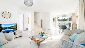 Un salón amplio con televisor, sofá, mesa de centro y una escalera que sube a un piso superior.