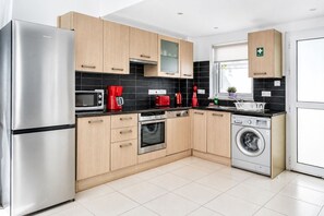 A modern kitchen with stainless steel appliances, wooden cabinets, and a black tiled backsplash. - Narcissos Villa Doria (Protaras)