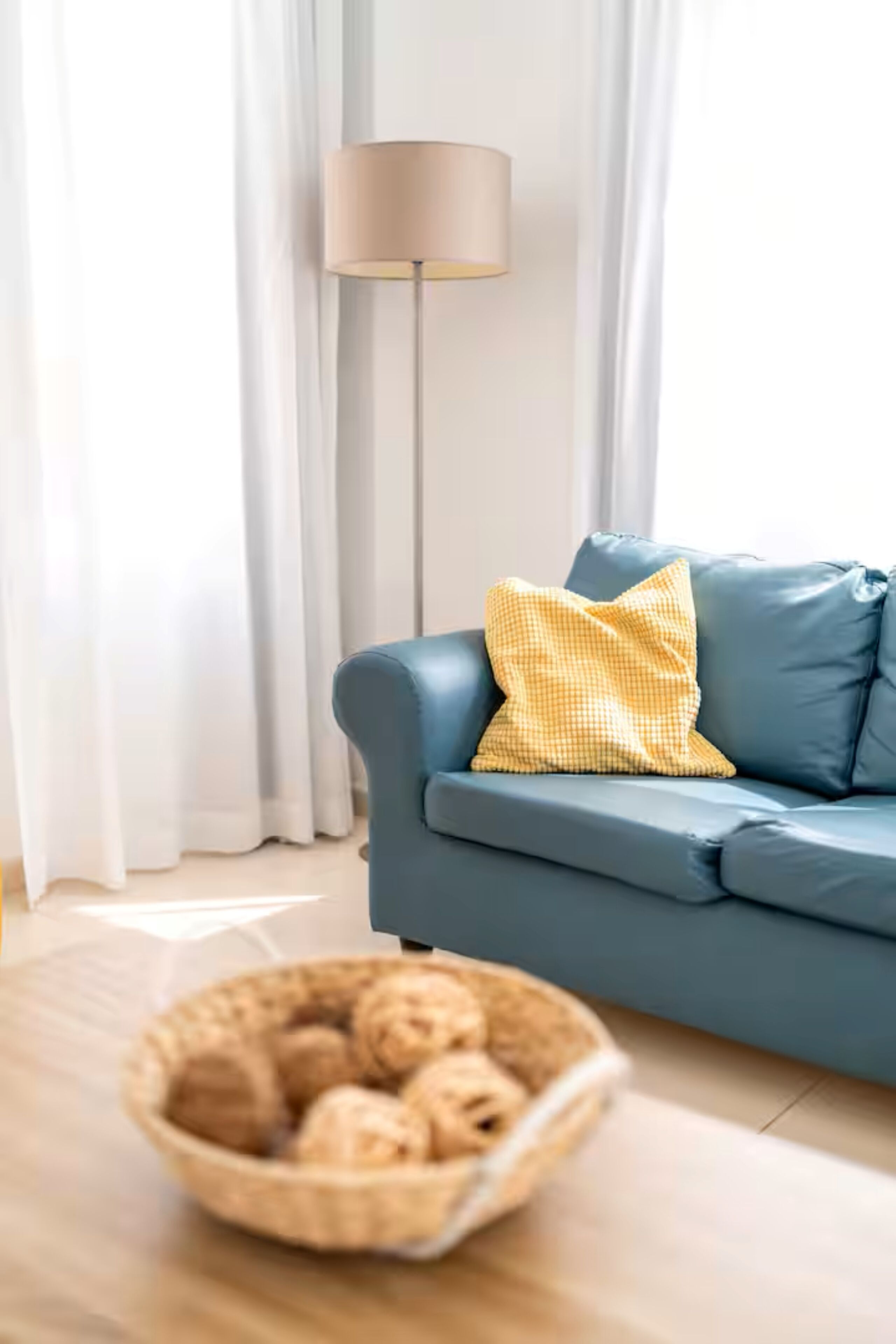 Ein Wohnzimmer mit einem blauen Sofa, einer Lampe und einem Korb voller Gegenstände auf dem Boden.