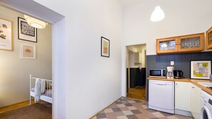 A compact kitchen with a microwave, coffee maker, and dishwasher. There is a small rug leading to a bed with a white headboard.