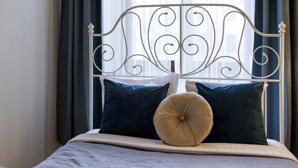 A bed with a white metal frame, dark blue pillows, and a beige accent pillow.