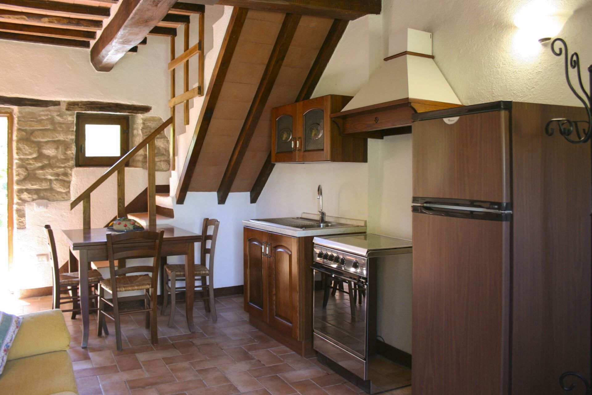 A kitchen with a stove, refrigerator, wooden cabinets, and a dining area with chairs.