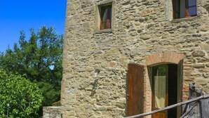 Ein Steinhaus mit einer Holztür und -fenstern, einer Treppe und einem Metallgeländer.