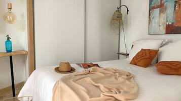 A neatly made bed with a beige blanket, a straw hat, and a magazine on the nightstand.