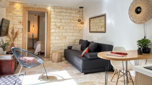 A modern living room with a stone wall, a black sofa, a round wooden table, and a woven light fixture. - Home Chic Home - La Terrasse Bazille (Montpellier)