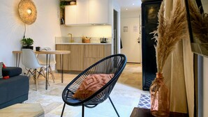 A modern living room with a black chair, a sofa, a dining table, and a kitchen area with white cabinets and a black refrigerator. - Home Chic Home - La Terrasse Bazille (Montpellier)
