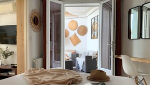 A bedroom with a bed, a hat, and a magazine on the bed. There is a door leading to another room with a sofa and a lamp. - Home Chic Home - La Terrasse Bazille (Montpellier)