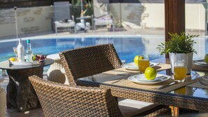 Una mesa de comedor con sillas de mimbre, un tablero de cristal y vistas a una piscina.