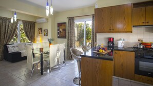 Una cocina moderna con armarios de madera, un comedor con mesa y sillas de vidrio, y un ventanal con cortinas.