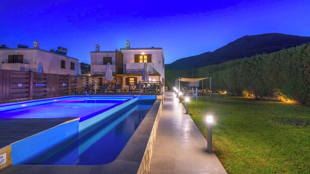A swimming pool with a pathway leading to a building with multiple windows and a covered outdoor seating area. - Lindos Topaz - Two Bedroom Villa, Sleeps 4 (Lindos)