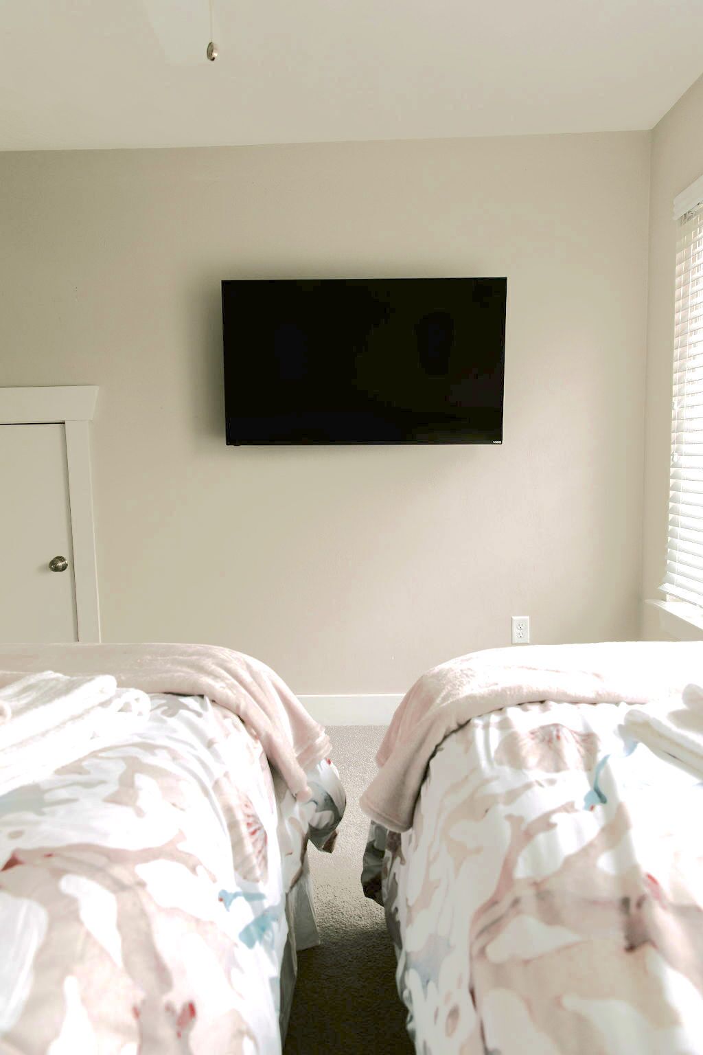 A bedroom with two beds, a television mounted on the wall, and a door to the left.