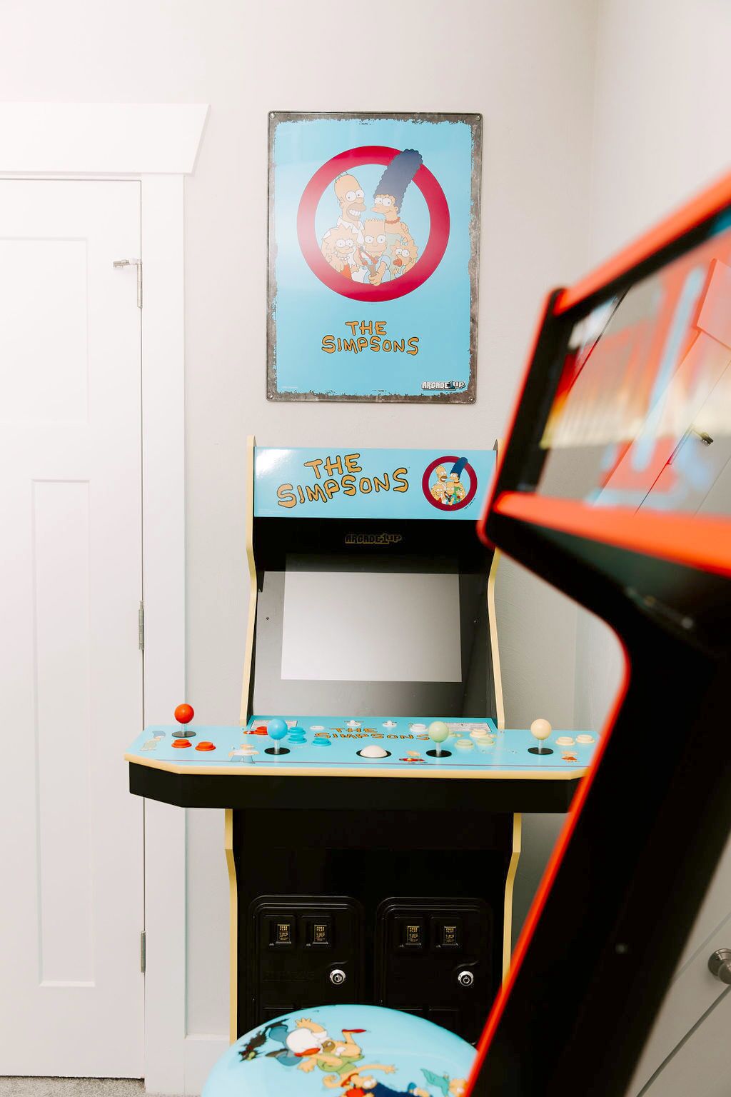 A room with a Simpsons arcade machine, a door, and a wall-mounted TV.