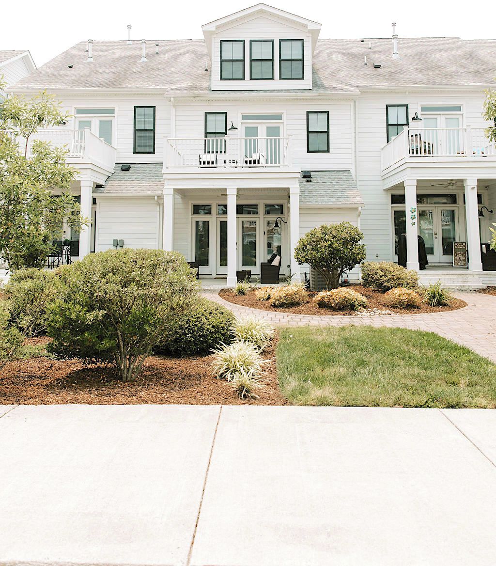 A two-story building with a central entrance, a covered porch, and a small garden area with shrubs and a lawn.