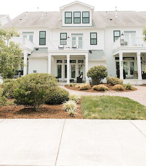 A two-story building with a central entrance, a covered porch, and a small garden area with shrubs and a lawn.