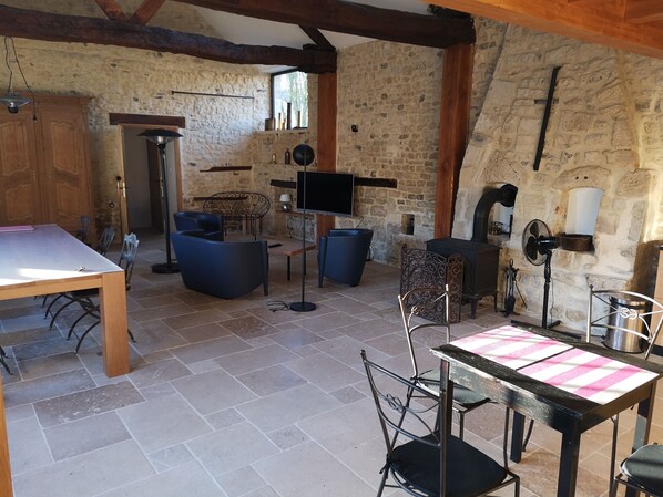 Une pièce rustique aux murs de pierre, avec une table en bois, des chaises bleues, un téléviseur et une cheminée.