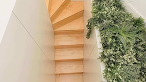 A wooden staircase with a white wall and a green plant wall on the right.