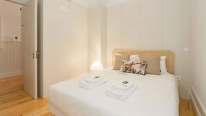 A neatly made bed with white linens and a headboard, a bedside lamp, and a door to the left.