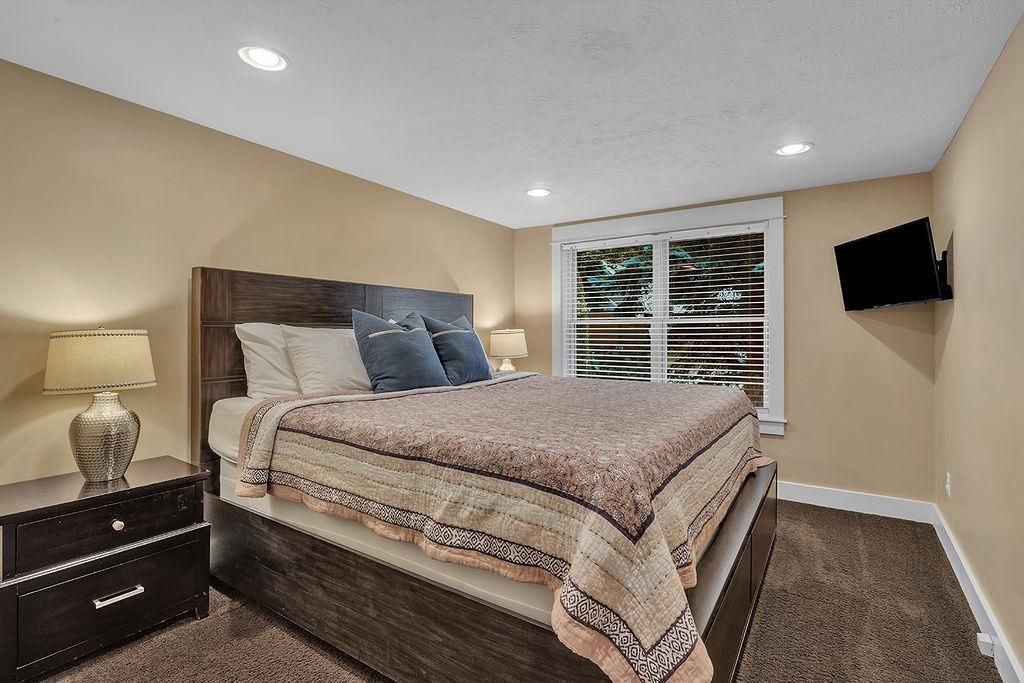 A bedroom with a bed, bedside table, lamp, and a TV mounted on the wall.