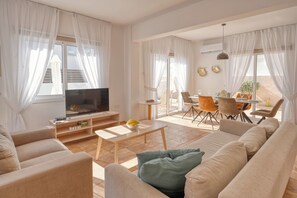 Uma sala de estar ampla com televisão de tela plana, um sofá, uma mesa de centro e um espaço de jantar com cadeiras e uma mesa.