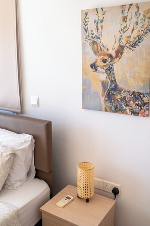 A bedroom with a bed, a bedside table with a lamp, a remote control, and a wall painting of a deer.