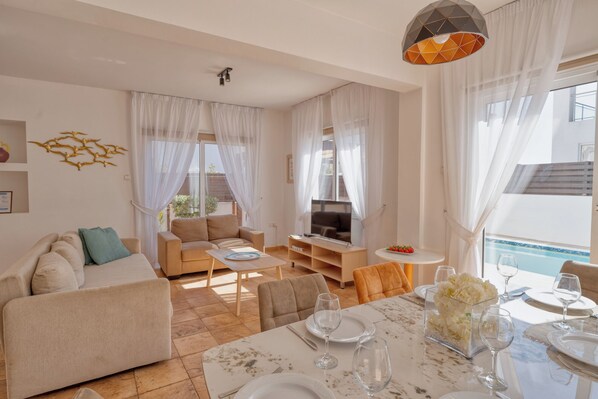 Uma sala de estar moderna com um sofá, uma televisão e um espaço de jantar com uma mesa posta para dois.