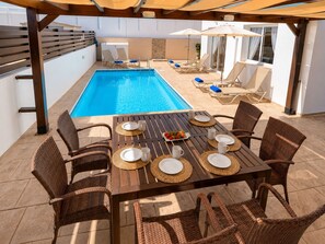 A poolside area with a rectangular pool, lounge chairs, and a dining table set for four.