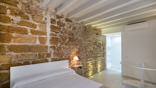 Una camera da letto con parete in pietra, un letto, un comodino con una lampada e una ringhiera bianca.