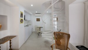 Una cucina moderna con mobili bianchi, un tavolo da pranzo e una sedia. Si nota una scala a chiocciola che conduce a un piano superiore.