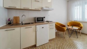 Eine kompakte Küche mit Mikrowelle, Spüle und kleinem Kühlschrank. Zwei gelbe Stühle und ein kleiner Tisch sind vorhanden.