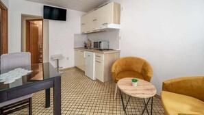 Ein gemütlicher Wohnbereich mit einer Küchenzeile, einem Esstisch mit Stühlen und einem kleinen, runden Tisch mit einer Pflanze.