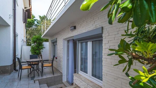 Ein kleiner Patio-Bereich mit Tisch und Stühlen, einem Blumentopf und einem Fenster mit Blick auf die Straße.