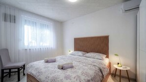 Ein Schlafzimmer mit einem Bett, einem Sessel, einem Nachttisch und einem Fenster mit Vorhängen.