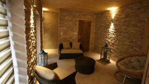 Ein gemütliches Zimmer mit Steinwand, Holzbalkendecke, einer Couch, einem Sessel und zwei Laternen.