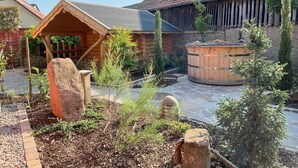 Eine rustikale Holzhütte mit Steinterrasse, Holz-Hot-Tub und einem umzäunten Garten.
